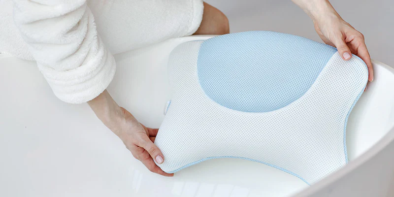 Frau platziert das blaue Badewannenkissen M von vesta+ in eine Badewanne, demonstriert ergonomisches Design und Komfort.